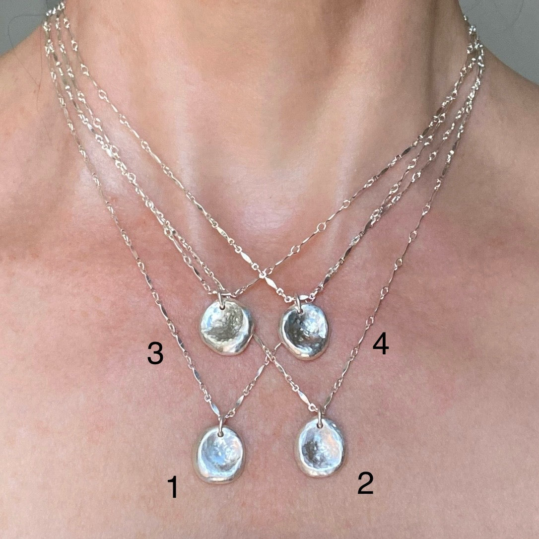 Three silver necklaces with pendant drops on a person's neck.