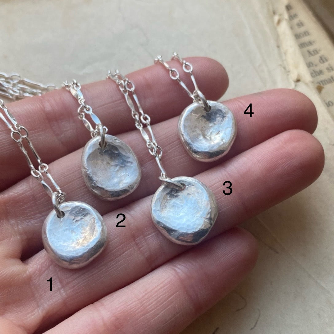 Four silver pendant necklaces on a hand with numbers indicating their order.